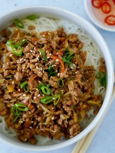 a white bowl filled with noodles and meat on top of a table next to chopsticks