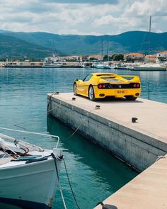 a yellow sports car is parked at the end of a dock next to a boat