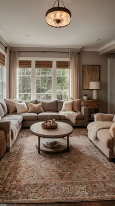 Cozy living room featuring a neutral-toned sectional sofa, vintage area rug, wooden coffee table, and natural light streaming through large windows with soft curtains. Cozy And Inviting Living Room, Living Room Remodel Cozy, Home Inspo Cozy Living Room, Warm And Inviting Living Room, Large Sofas Living Room, Warm Wood Floors Living Room, Colonial House Living Room, Bright Cozy Living Room, Cozy Lounge Room