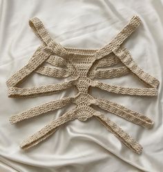 a crocheted piece of clothing laying on top of a white bed coverlet