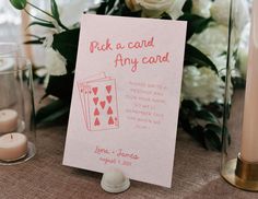 a pink card is sitting on a table next to some candles and vases with flowers