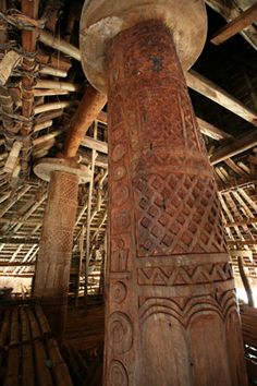 an old wooden pole with carvings on it in a room filled with bamboo poles and wood beams