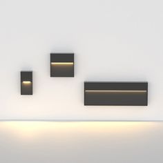 three square lights are lit up on the wall above a bench in a white room