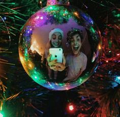 an ornament hanging from a christmas tree with two people holding a cell phone