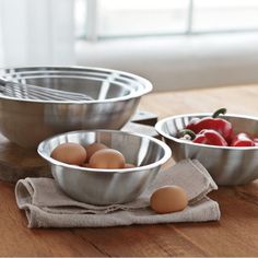 three metal bowls filled with eggs on top of a wooden table