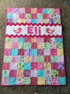 a pink and green quilt with the word ellie on it's side, next to a pair of baby shoes