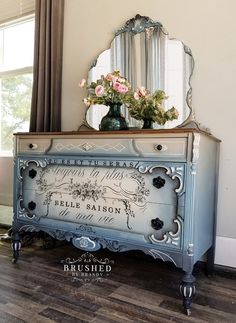 a blue dresser with flowers on top and a mirror above it