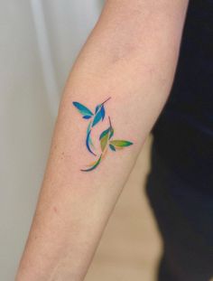 a colorful humming bird tattoo on the left forearm and right arm, with two small blue birds flying around it