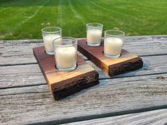 three shot glasses on a wooden tray with some milk in them sitting on a picnic table