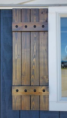 a window with wooden shutters on the side of a blue building next to a white door