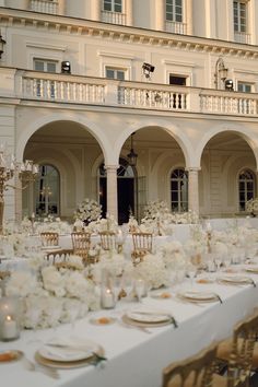 the tables are set with white flowers and place settings for an elegant wedding reception in front of a large building