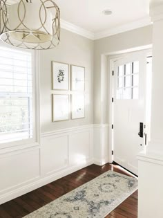 a hallway with white walls and wooden floors, framed pictures on the wall, and a rug