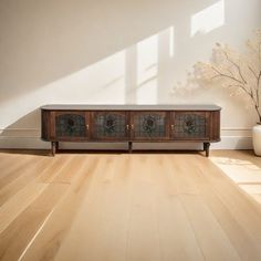 a wooden cabinet sitting on top of a hard wood floor next to a potted plant