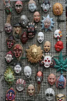 many different masks are on display in front of a wall with metal grates and wire