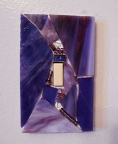 a light switch cover with purple and white tiles on the back ground, as well as a beaded cord