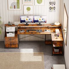 a desk with two computers on it in front of some pictures and a potted plant