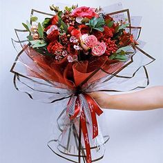 a hand holding a bouquet of flowers with red ribbon around it's wrist and wrapped in clear cellophane