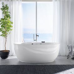 a large white bath tub sitting in front of a window next to a potted plant