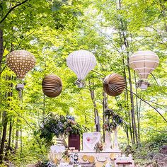 an outdoor wedding setup in the woods with paper lanterns and flowers on it, surrounded by greenery