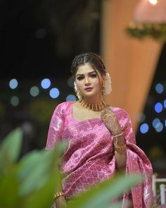 a woman in a pink sari and gold jewelry is standing outside at night with her hand on her hip