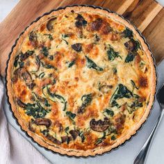 a quiche with cheese and spinach on a cutting board next to a fork