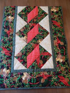 a quilted table topper with red and green ribbons on it's edges