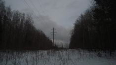 an empty road with power lines in the distance and snow on the ground near trees