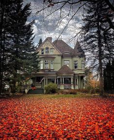 an old victorian house surrounded by trees and leaves on the ground in front of it