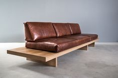 a brown leather couch sitting on top of a wooden table next to a gray wall