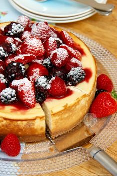 a cheesecake with berries and powdered sugar on top sits on a glass plate