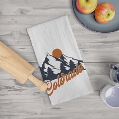 a kitchen towel with the words colorado on it next to two apples and a teapot