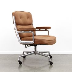 an office chair with a brown leather upholstered seat and chrome frame, in front of a white wall