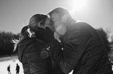 a man and woman are kissing in the snow on a sunny day with other people behind them