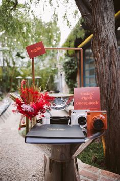 a table with a camera and some flowers on it next to a tree in front of a building