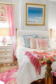 a white bed with pink and blue comforters in a bedroom next to a window