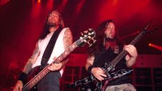 two men with long hair playing guitars on stage