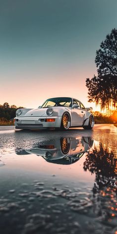 a white sports car parked on the side of a lake at sunset with trees in the background