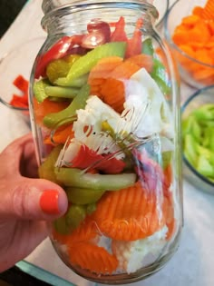 a person is holding up a jar full of vegetables and other foods in the background