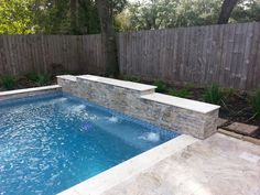 a small swimming pool in the middle of a backyard with a stone wall around it