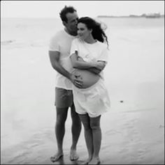 a man and woman hugging each other on the beach while holding a baby in their arms