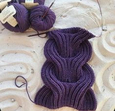 two balls of yarn are laying next to each other on the sand and one is purple