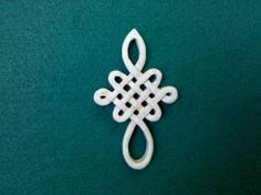 a white brooch with an intricate design on the front and back of it, sitting on a green surface