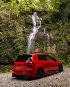 a red car parked in front of a waterfall