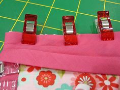 three red clips are placed on top of a pink fabric with flower print pattern and green background