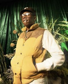 a man in a yellow vest and hat standing with his hands on his hips while wearing glasses