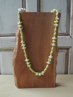 a wooden stand holding a necklace with white and green flowers hanging from it's sides