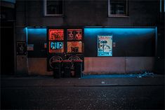 a dark city street at night with neon signs on the building and trash cans in front