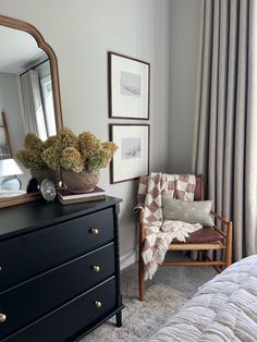 a bedroom with a dresser, mirror and chair in it's corner next to a window