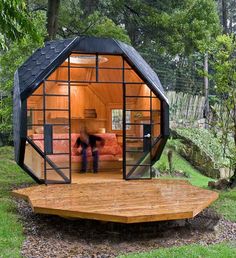 a small cabin in the middle of a forest with two people standing inside and looking at it