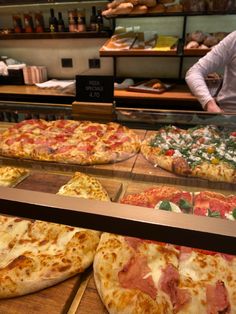 several different types of pizzas on display in a bakery case, including one with ham and cheese